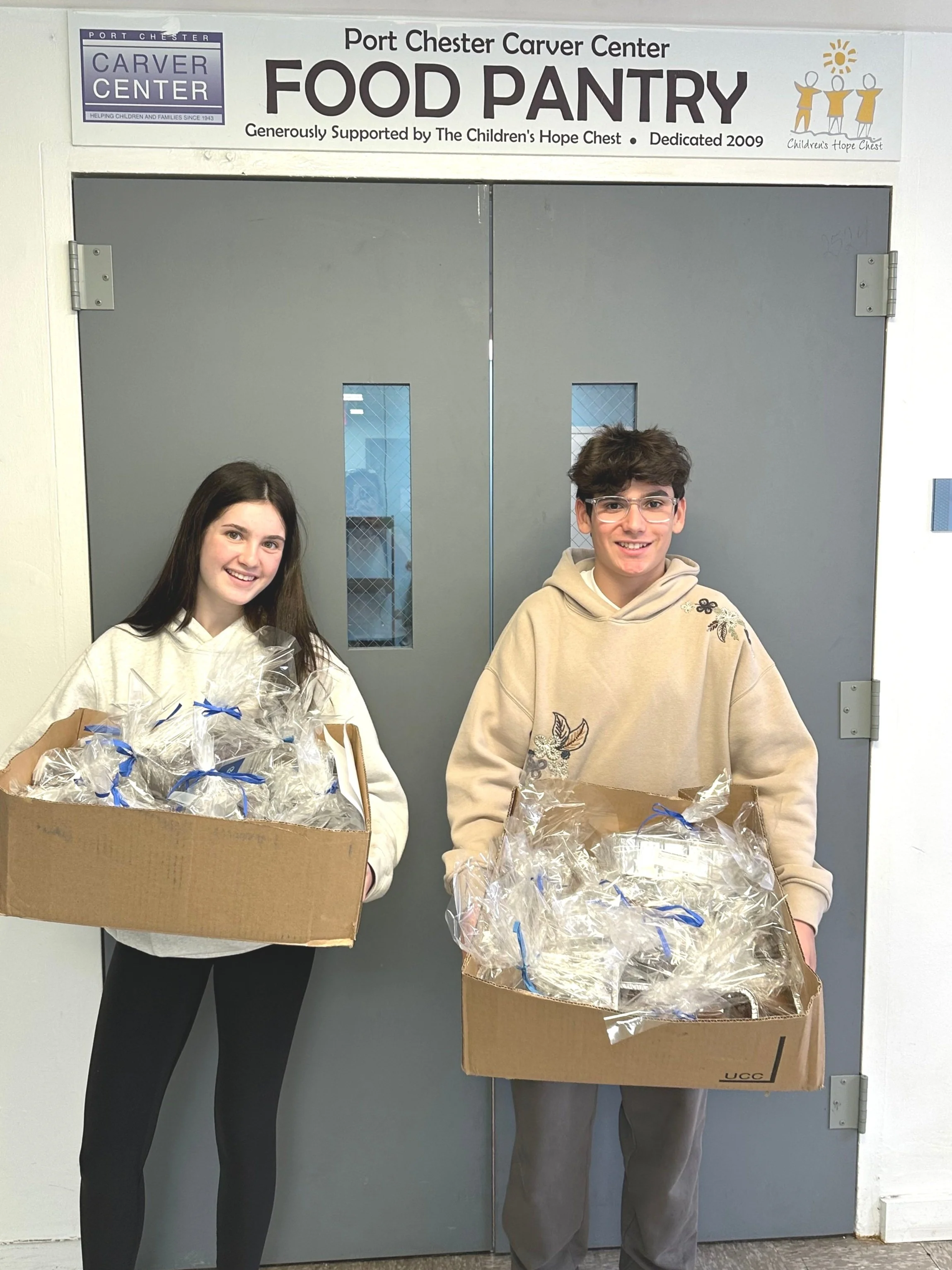 Two PeaceofCakes volunteers holding boxes of wrapped cakes at the Port Chester Carver Center Food Pantry