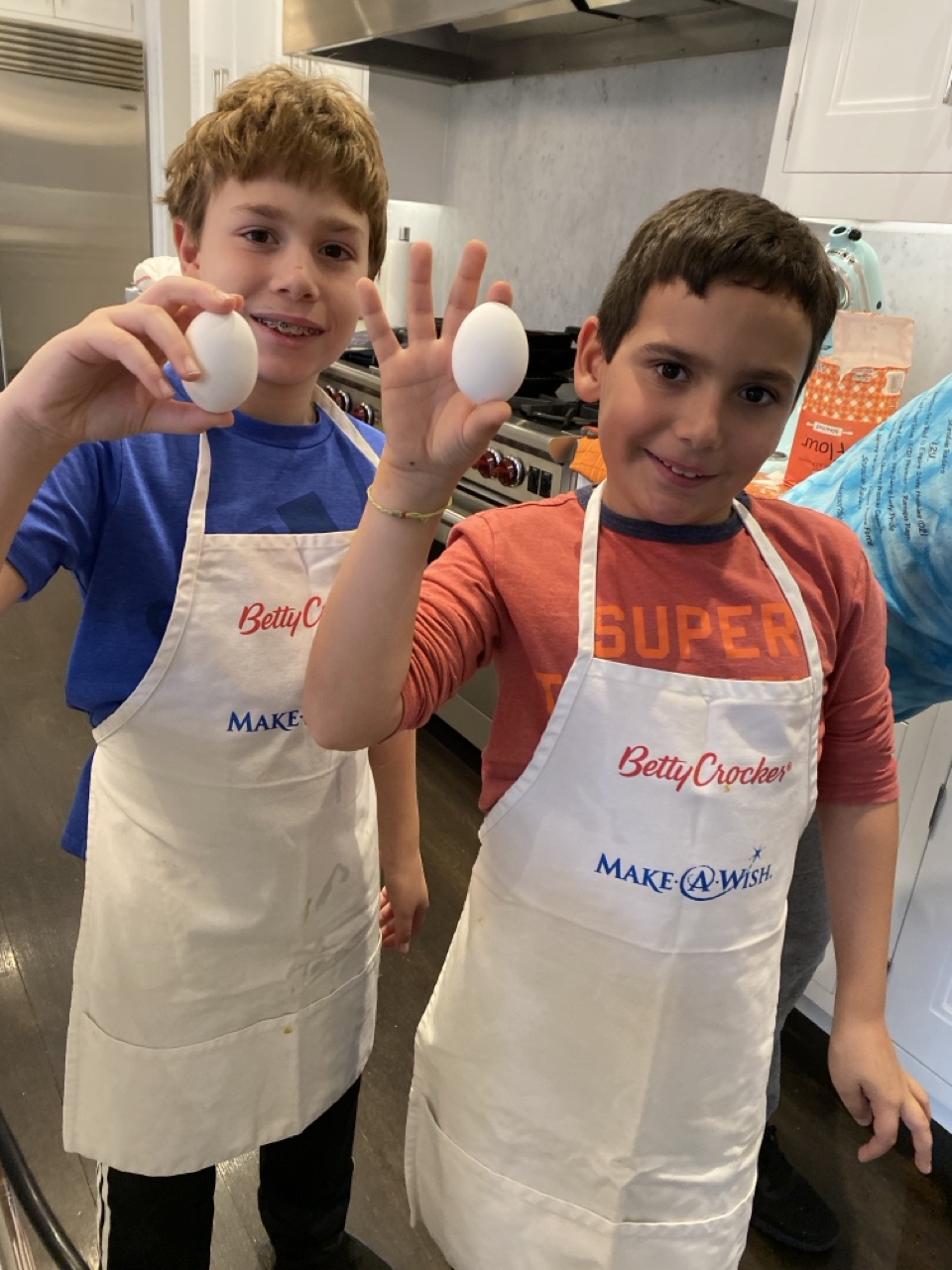 Two young PeaceofCakes bakers in aprons holding eggs in a kitchen